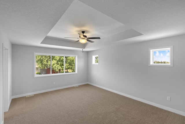 carpeted empty room featuring visible vents, baseboards, a ceiling fan, a raised ceiling, and a textured ceiling