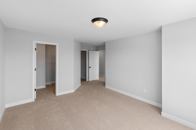 unfurnished bedroom with a walk in closet, a closet, light colored carpet, and baseboards