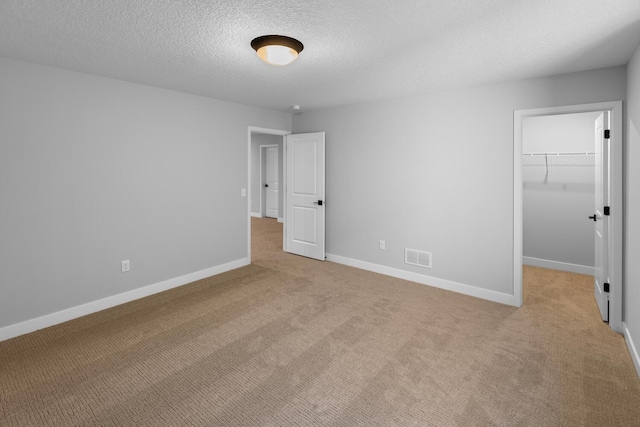 unfurnished bedroom featuring light carpet, a spacious closet, visible vents, and baseboards