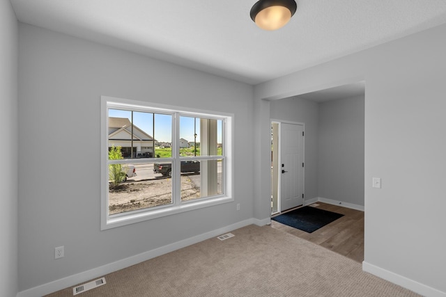 foyer entrance featuring carpet floors, visible vents, and baseboards