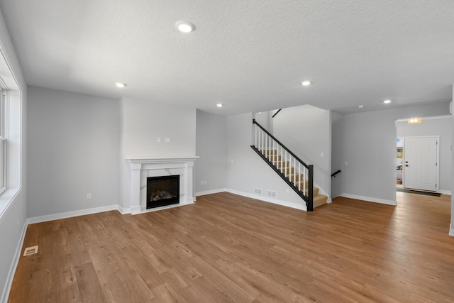 unfurnished living room with light wood-type flooring, visible vents, a premium fireplace, and stairs