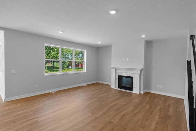 unfurnished living room featuring baseboards, a glass covered fireplace, a textured ceiling, light wood-type flooring, and recessed lighting