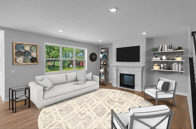 living area featuring a glass covered fireplace, recessed lighting, baseboards, and wood finished floors