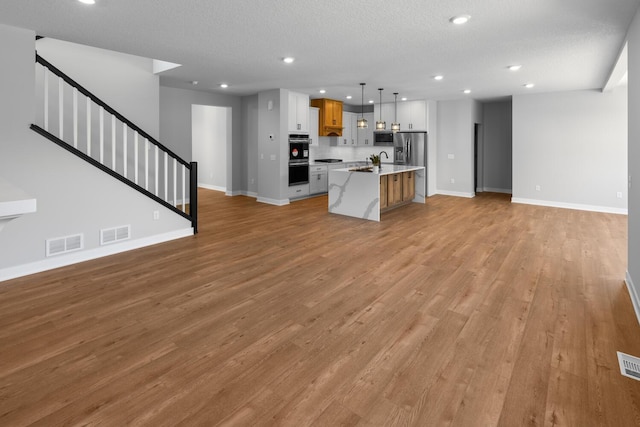 unfurnished living room with stairs, light wood-type flooring, visible vents, and recessed lighting