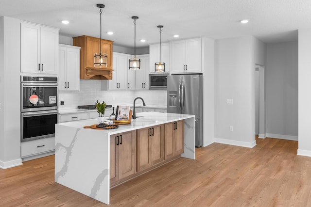 kitchen featuring stainless steel appliances, backsplash, light wood finished floors, a center island with sink, and pendant lighting