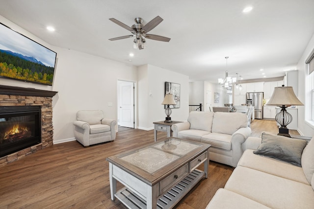 living room with ceiling fan with notable chandelier, a stone fireplace, and dark hardwood / wood-style floors