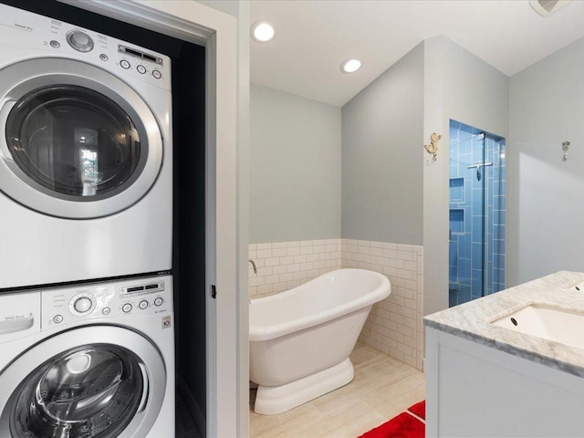 clothes washing area with a wainscoted wall, stacked washing maching and dryer, laundry area, a sink, and tile walls