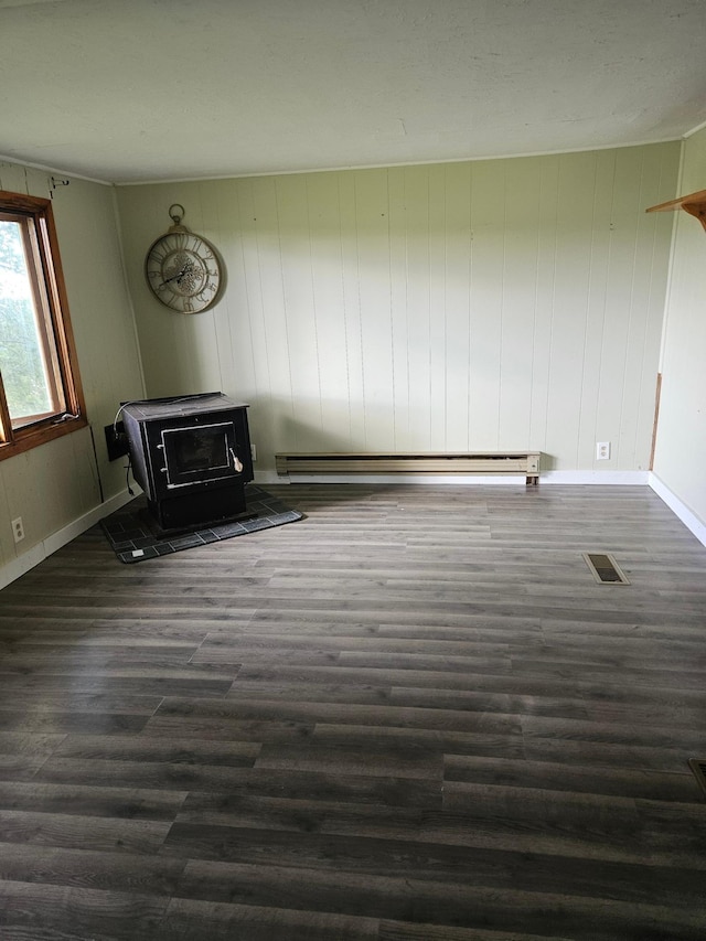 empty room featuring wood walls, a baseboard radiator, a wood stove, and dark hardwood / wood-style flooring