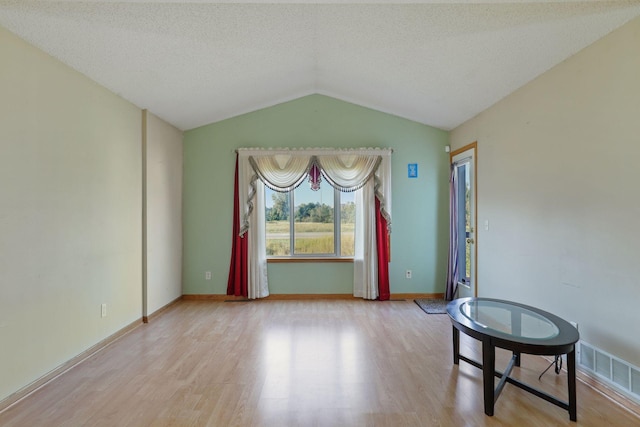 spare room with light hardwood / wood-style flooring, lofted ceiling, and a textured ceiling