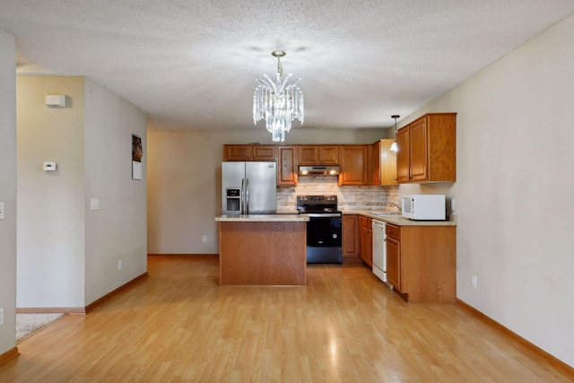 kitchen with a textured ceiling, hanging light fixtures, a kitchen island, light hardwood / wood-style flooring, and white appliances