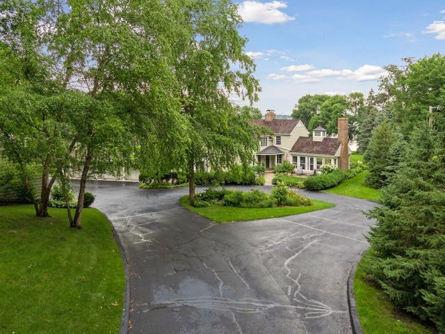 view of front facade with driveway, a chimney, and a front yard