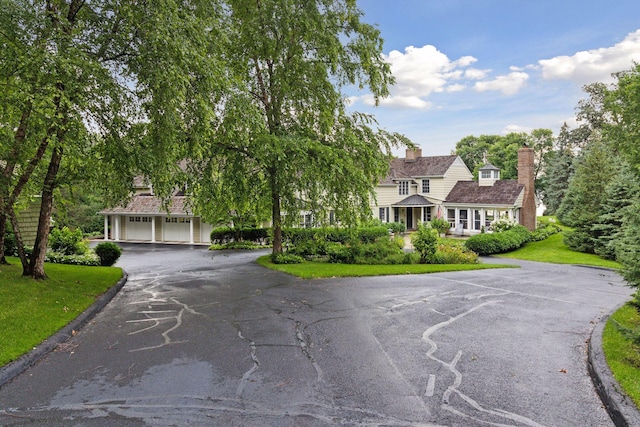 view of front of property featuring a front yard, a chimney, a garage, and aphalt driveway