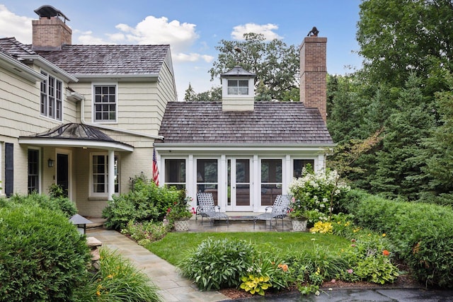 view of front of house with a patio, brick siding, and a chimney