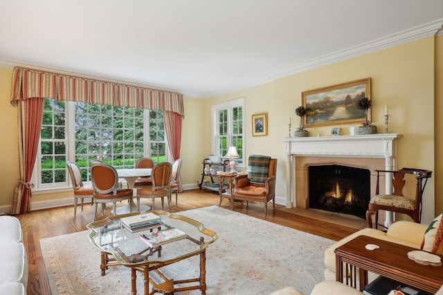 living area with a fireplace with flush hearth, crown molding, baseboards, and wood finished floors