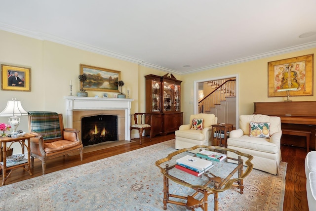 living area featuring a fireplace with flush hearth, stairs, crown molding, and wood finished floors