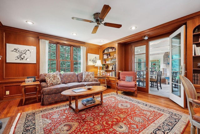 living room with wooden walls, built in shelves, wood finished floors, and ceiling fan