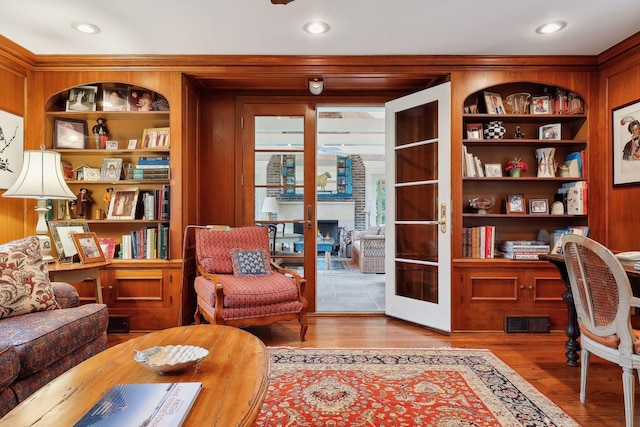 sitting room with built in features, visible vents, a lit fireplace, and wood finished floors