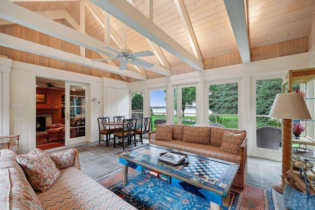 sunroom featuring ceiling fan, wooden ceiling, vaulted ceiling with beams, and a lit fireplace