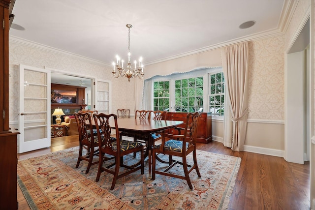 dining room featuring wallpapered walls, crown molding, wood finished floors, and baseboards