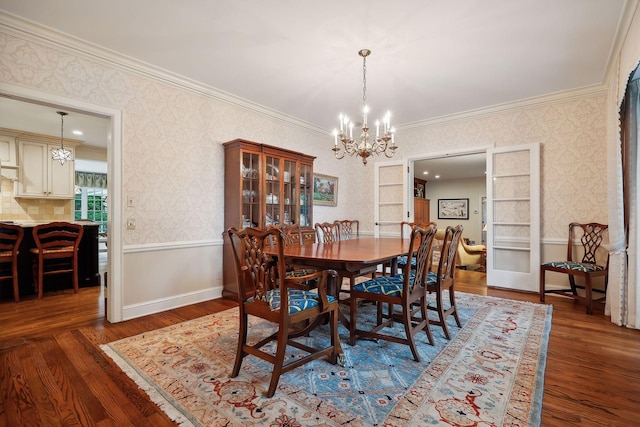 dining space featuring wood finished floors, a wainscoted wall, wallpapered walls, crown molding, and a notable chandelier