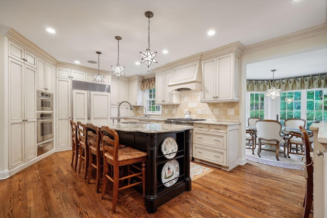 kitchen with premium range hood, light stone counters, wood finished floors, a warming drawer, and a sink