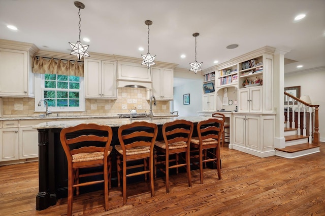 kitchen featuring a center island with sink, crown molding, and light wood finished floors