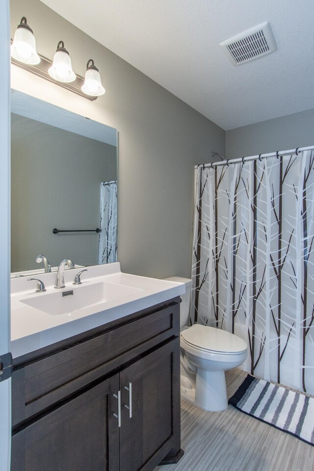 bathroom with walk in shower, vanity, hardwood / wood-style floors, and toilet