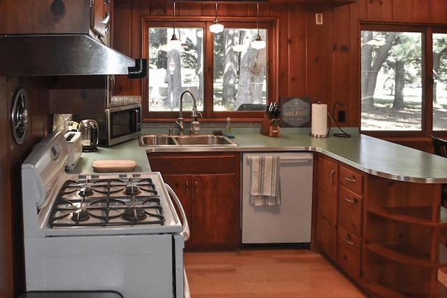 kitchen with light hardwood / wood-style flooring, white appliances, sink, kitchen peninsula, and wood walls