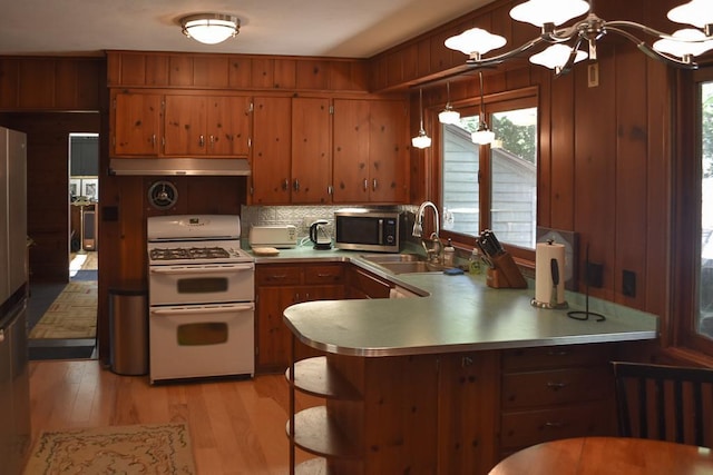 kitchen with pendant lighting, light hardwood / wood-style flooring, white gas range, kitchen peninsula, and decorative backsplash