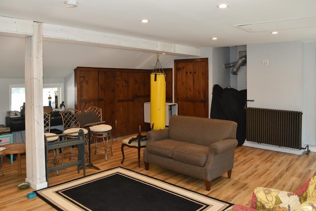 living room featuring radiator heating unit, beam ceiling, and light hardwood / wood-style floors