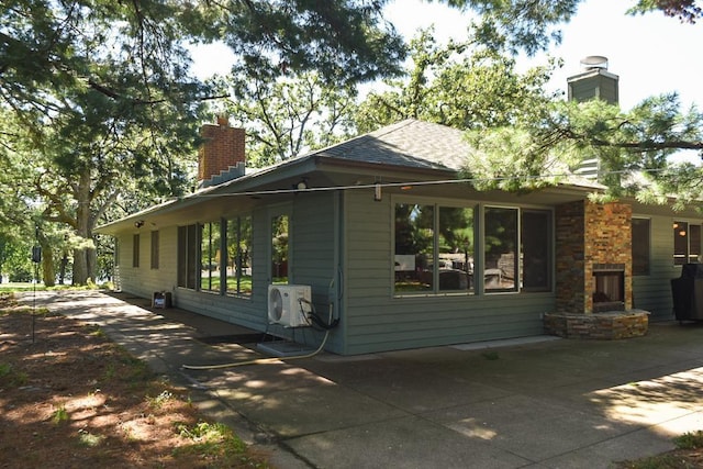 view of property exterior with ac unit, roof with shingles, a chimney, and a patio area