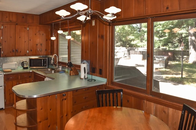 kitchen with stainless steel microwave, wooden walls, stainless steel countertops, brown cabinetry, and a sink