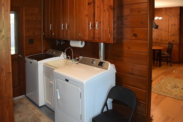 clothes washing area featuring cabinet space, light wood-style floors, wood walls, and washer and clothes dryer