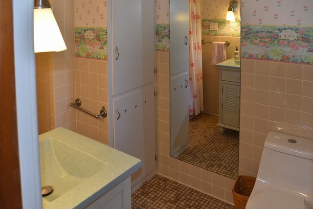 full bathroom with tile patterned flooring, wallpapered walls, a wainscoted wall, toilet, and tile walls