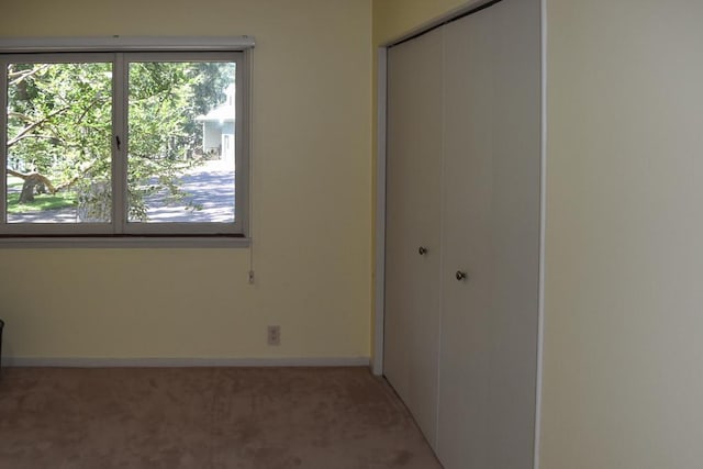 unfurnished bedroom with a closet, multiple windows, light colored carpet, and baseboards