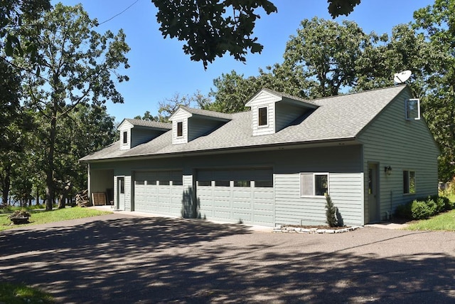 view of side of property featuring aphalt driveway, an attached garage, and a shingled roof