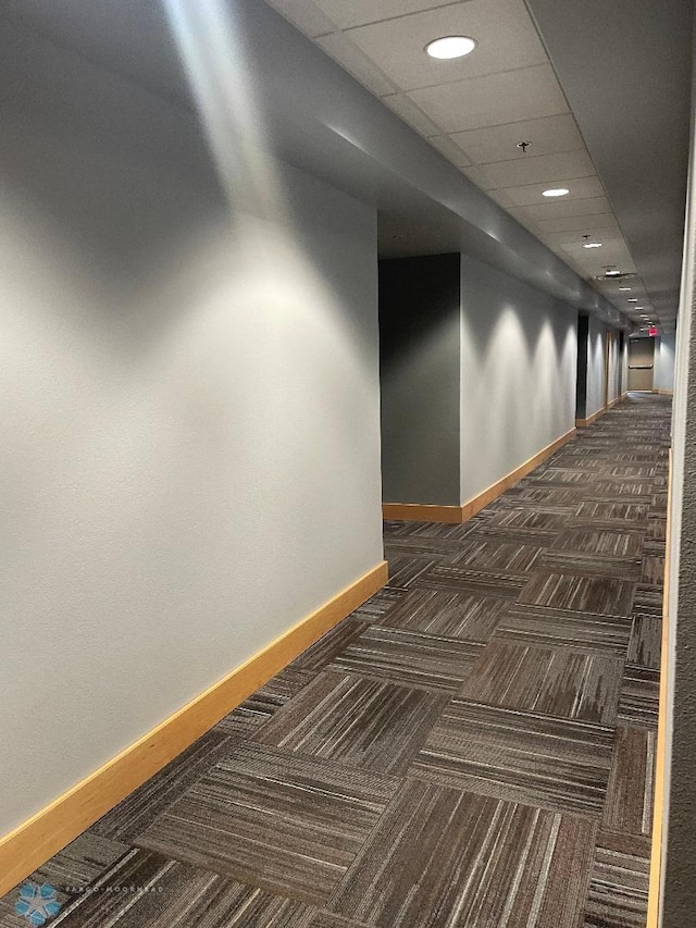 hall featuring a drop ceiling and dark colored carpet