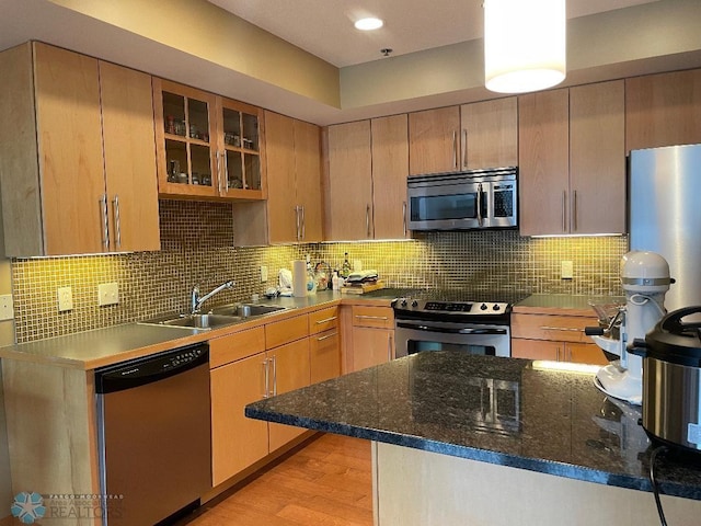 kitchen with decorative backsplash, light hardwood / wood-style floors, dark stone countertops, stainless steel appliances, and sink