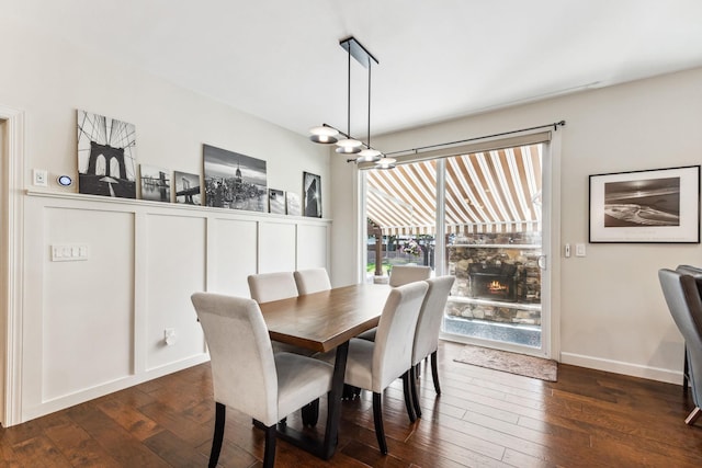 dining space with dark wood-style flooring, a stone fireplace, baseboards, and an inviting chandelier