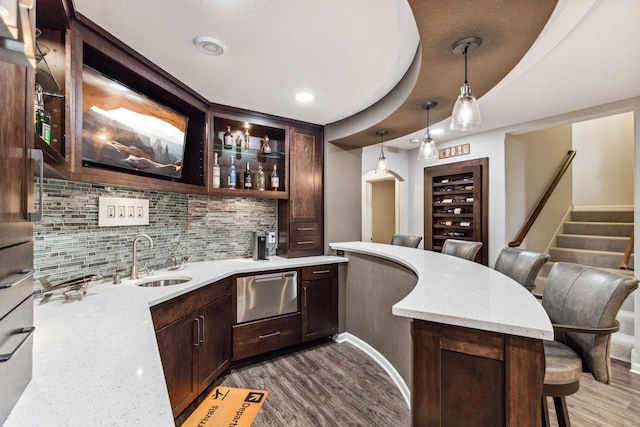 bar with light stone counters, sink, dark hardwood / wood-style floors, pendant lighting, and tasteful backsplash