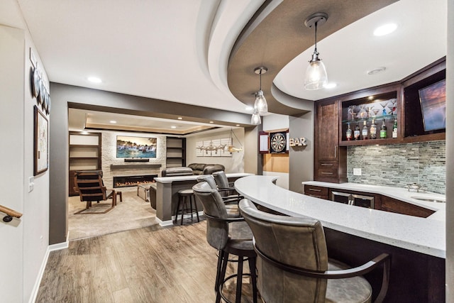 bar with a fireplace, decorative light fixtures, light stone countertops, light hardwood / wood-style floors, and tasteful backsplash