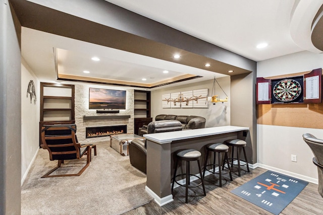 interior space with a large fireplace, a tray ceiling, wood finished floors, and baseboards