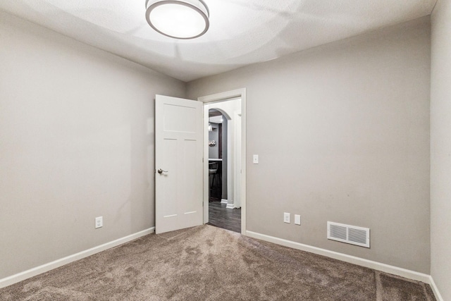 spare room featuring arched walkways, baseboards, visible vents, and carpet flooring