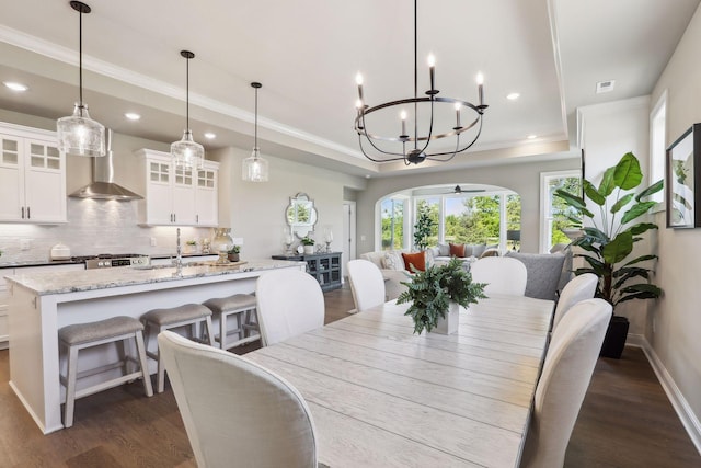 dining space with crown molding, ceiling fan with notable chandelier, dark hardwood / wood-style flooring, sink, and a tray ceiling