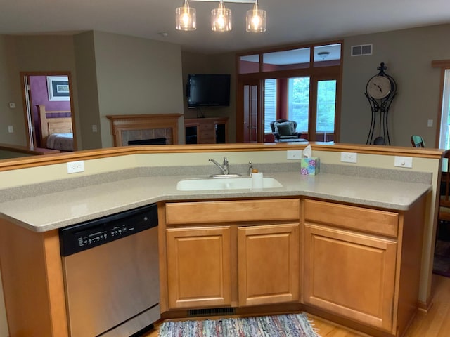 kitchen featuring pendant lighting, sink, dishwasher, a tile fireplace, and light wood-type flooring