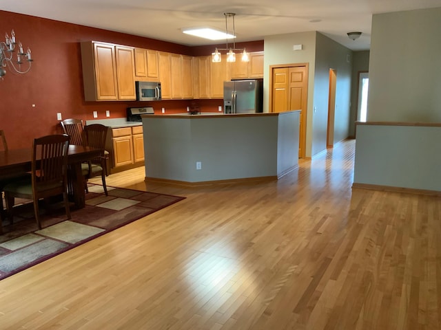 kitchen with appliances with stainless steel finishes, light brown cabinets, a center island, light hardwood / wood-style flooring, and decorative light fixtures