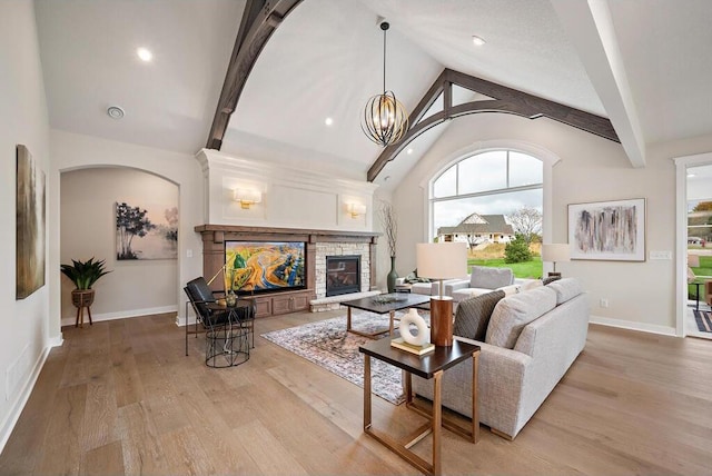 living room featuring light hardwood / wood-style floors, high vaulted ceiling, a fireplace, beamed ceiling, and a notable chandelier