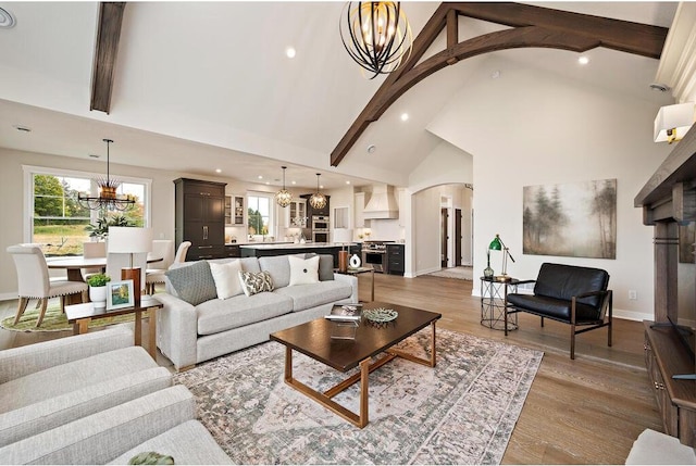 living room featuring a notable chandelier, beam ceiling, light hardwood / wood-style floors, and high vaulted ceiling