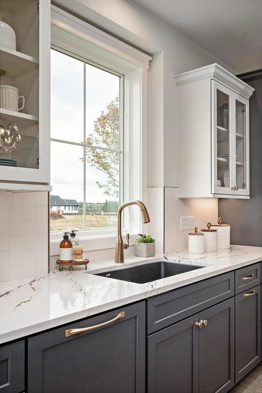 kitchen featuring gray cabinetry, white cabinets, backsplash, light stone countertops, and sink