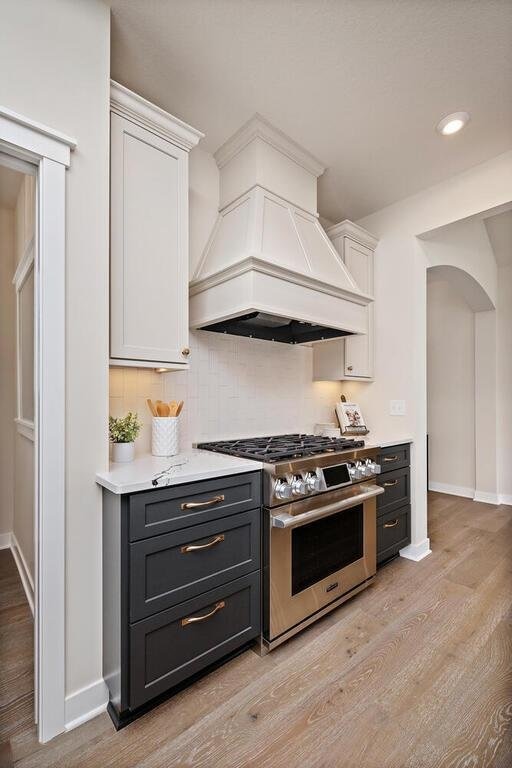 kitchen with light hardwood / wood-style floors, white cabinetry, backsplash, stainless steel range, and premium range hood